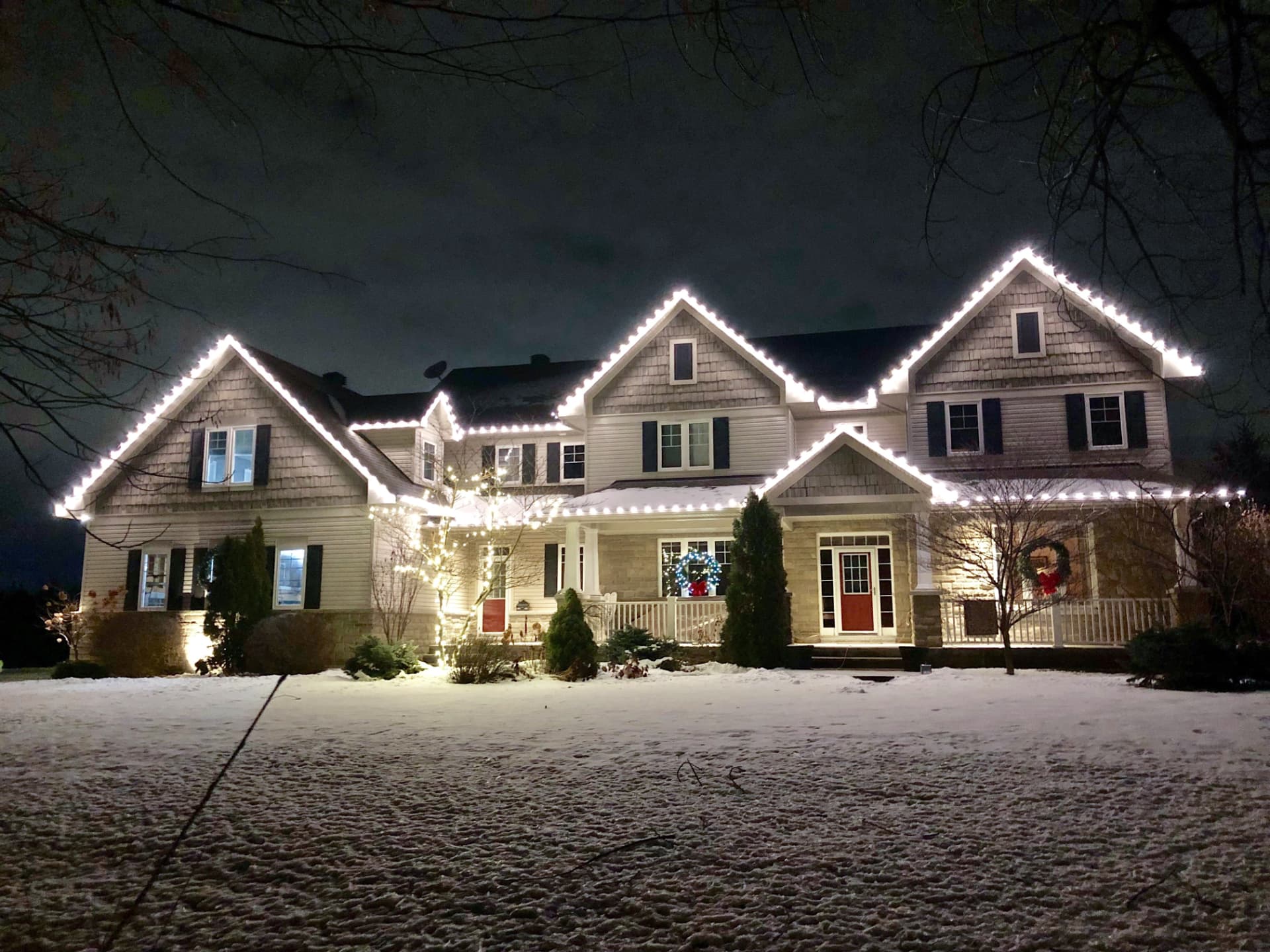Craftsman home wrapped in warm white holiday lights on a snowy evening
